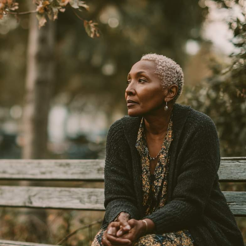 A thoughtful woman sits on a park bench, reflecting during online thought disorder counseling.